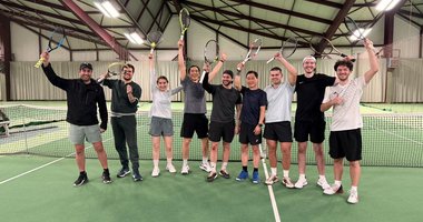 Gruppe von jungen Menschen die vor dem Tennisnetz ihre Schläger hochhält