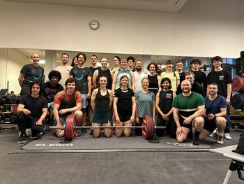 Gruppe von Athlet*innen hinter einer Hantel