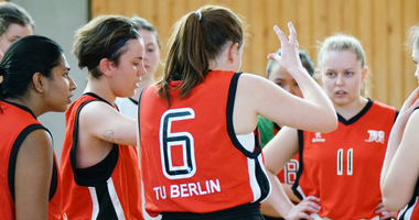 Frauen-Basketballteam in TU-roten Trikots berät sich in einer Runde