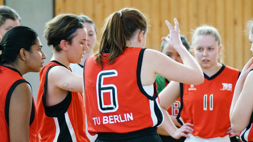 Frauen-Basketballteam in TU-roten Trikots berät sich in einer Runde