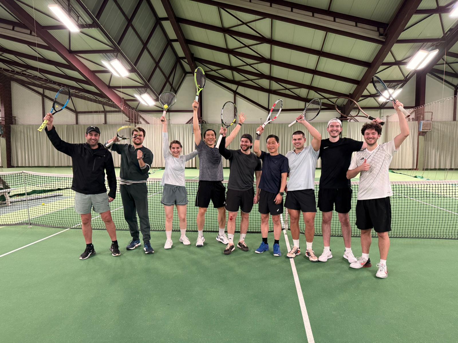 Gruppe von jungen Menschen die vor dem Tennisnetz ihre Schläger hochhält